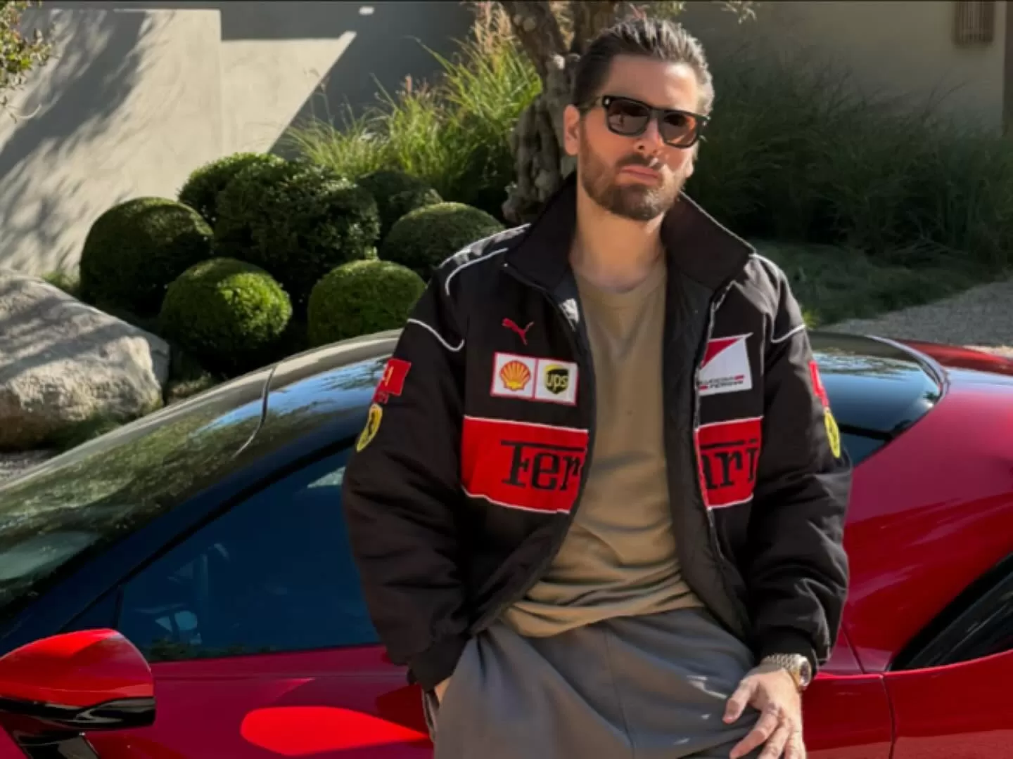 Scott Disick debout à côté de sa voiture rouge.