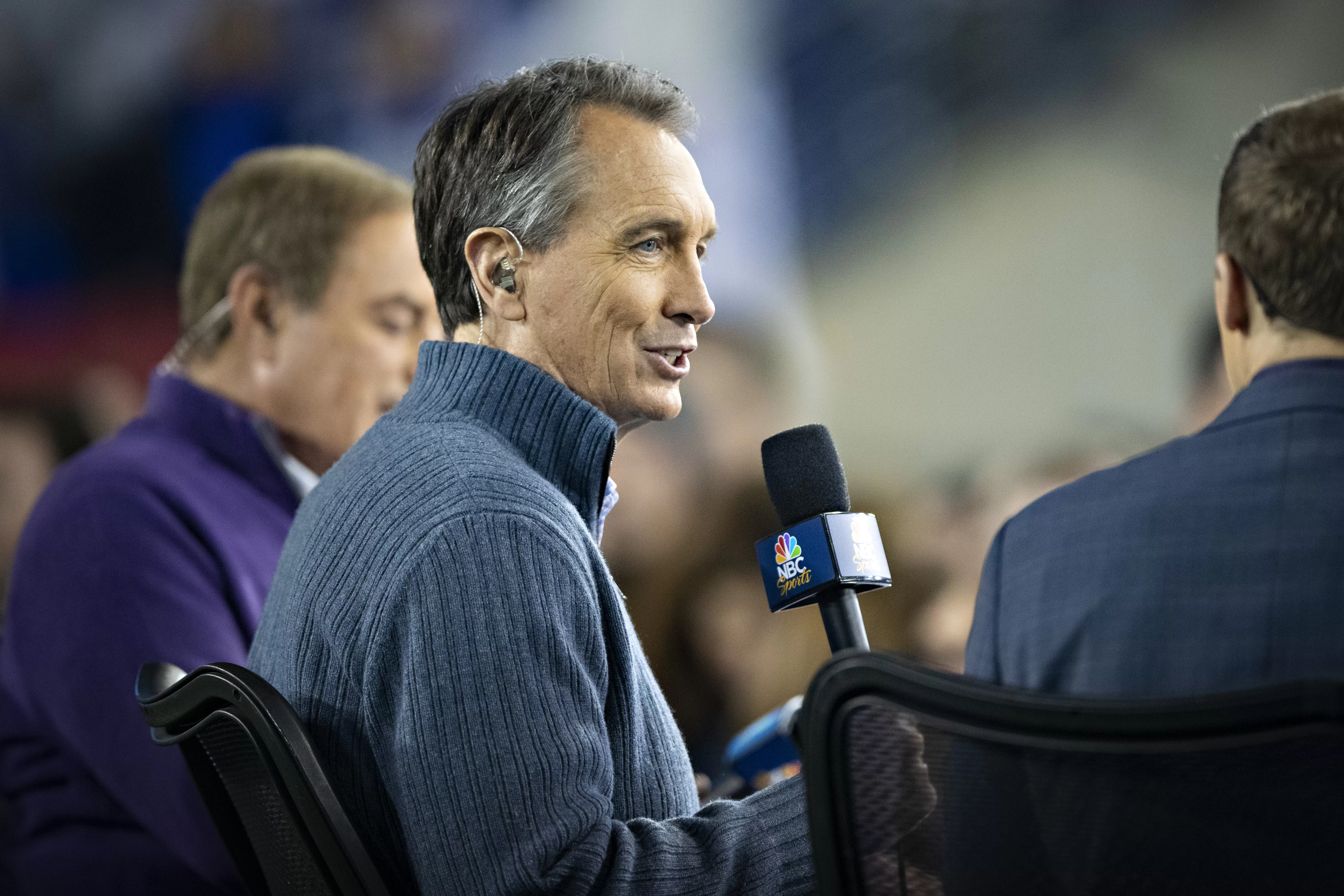 Cris Collinsworth at an NFL game, speaking into an NBC Sports microphone.